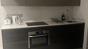 A modern kitchen with grey cabinets, a stainless steel sink, a built-in oven, and a countertop with a kettle and a bottle of dish soap.