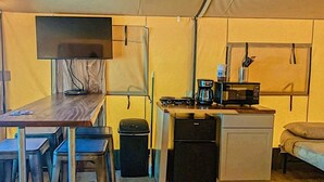 A compact kitchen area with a wooden table, two stools, a microwave, a coffee maker, and a small refrigerator. - Sons Rio Cibolo Safari Cabin 1 (Marion)
