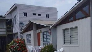 Ein zweigeschossiges Gebäude mit einer Veranda und einem kleinen Gartenbereich mit Blumen und Plastikstühlen.