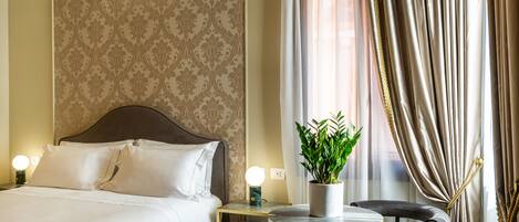 A hotel room with a large bed, bedside table, lamp, chair, and a potted plant.