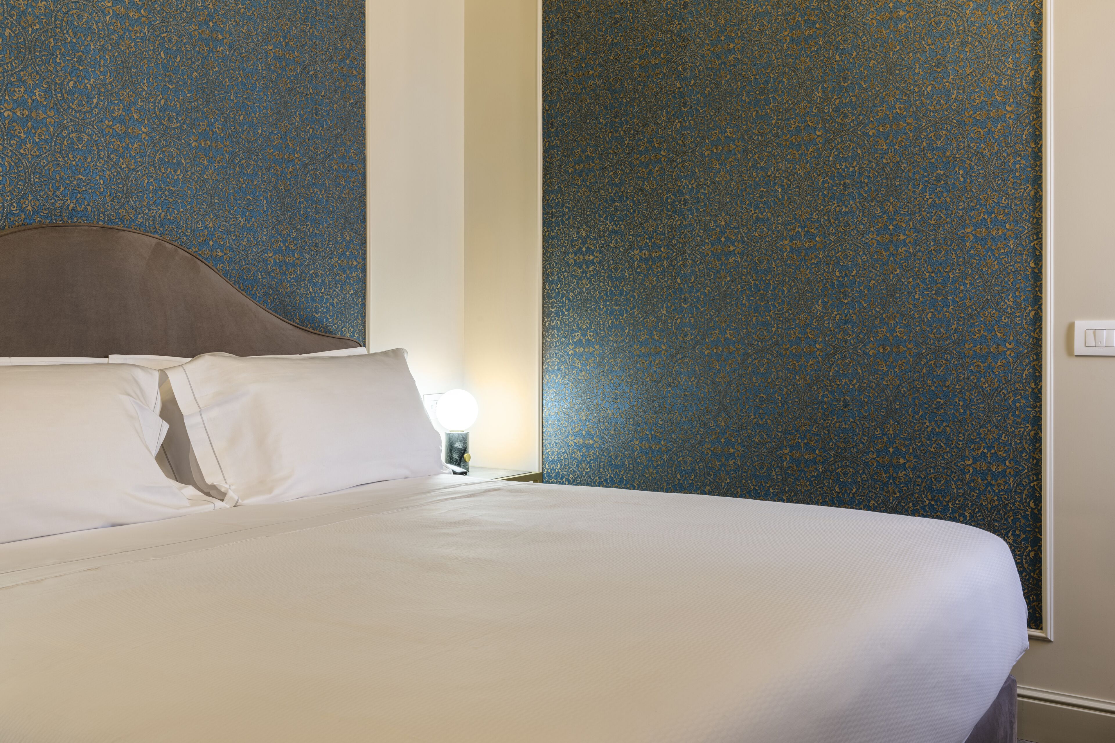 Una cama bien hecha con sábanas blancas en una habitación con papel tapiz estampado en azul.