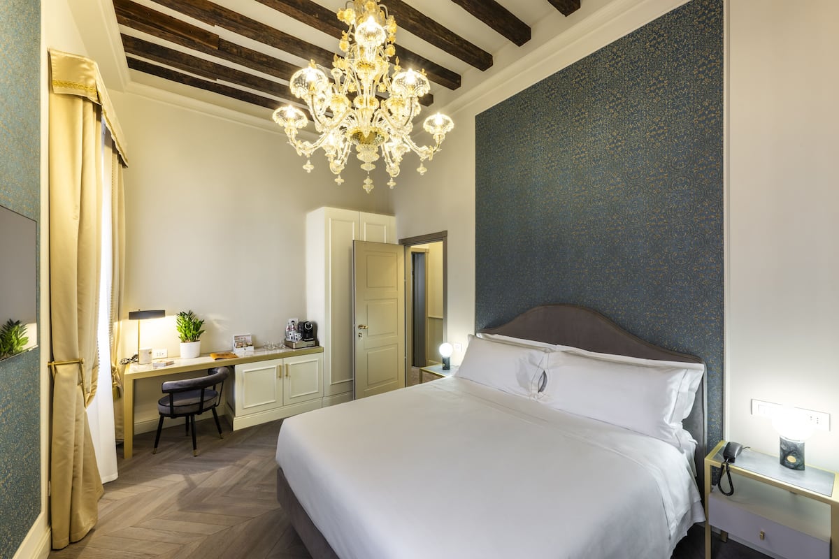 Une chambre d’hôtel avec un grand lit, un bureau avec une chaise, un lustre et une petite table de chevet avec une lampe.