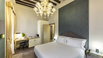 Habitación de hotel con una cama grande, un escritorio con una silla, una araña y una mesita de noche con lámpara.