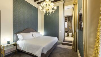Une chambre à coucher avec un grand lit, une table de chevet, un lustre et une salle de bain visible à travers une porte ouverte.