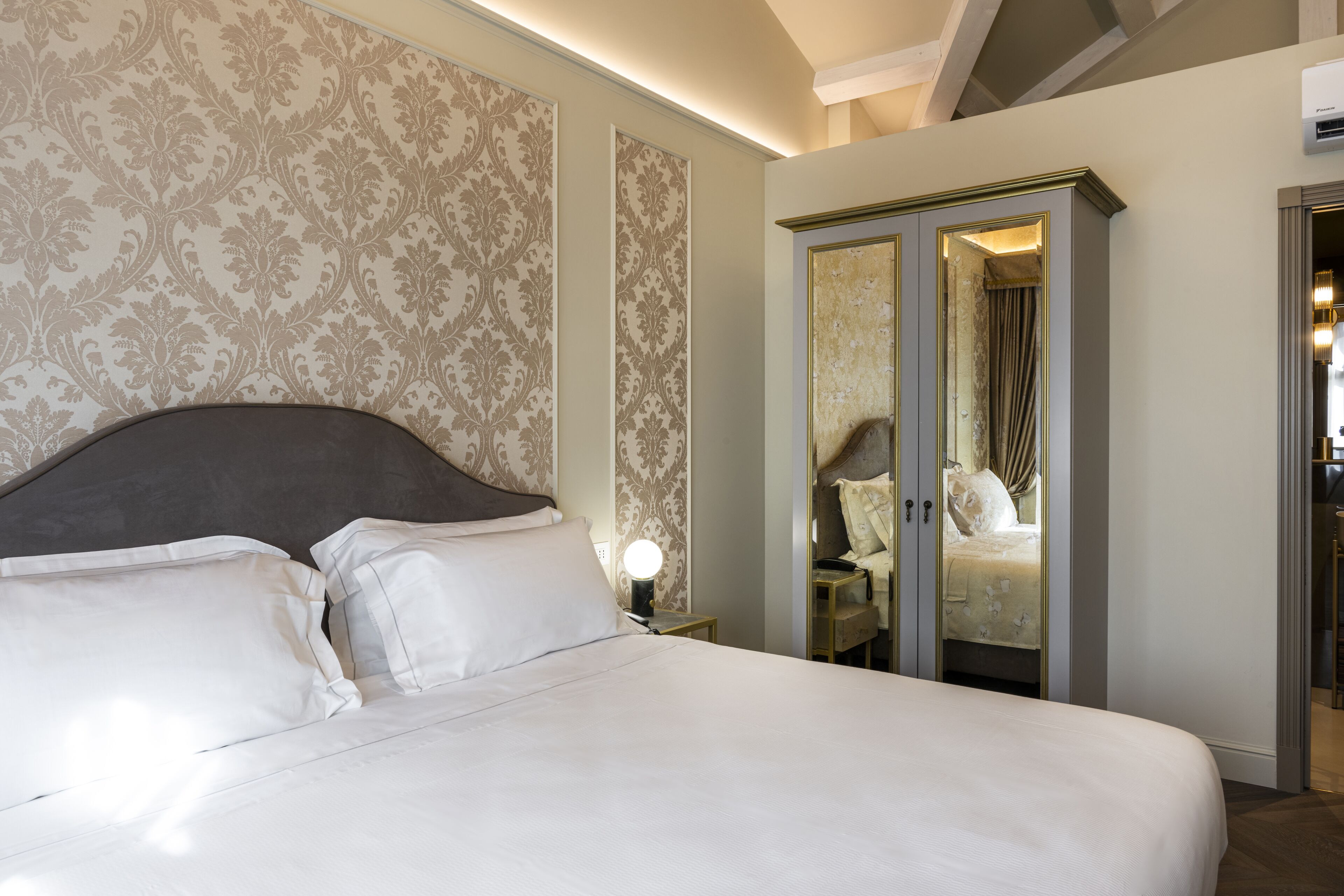 A neatly made bed with white linens, a headboard, and a nightstand with a lamp.