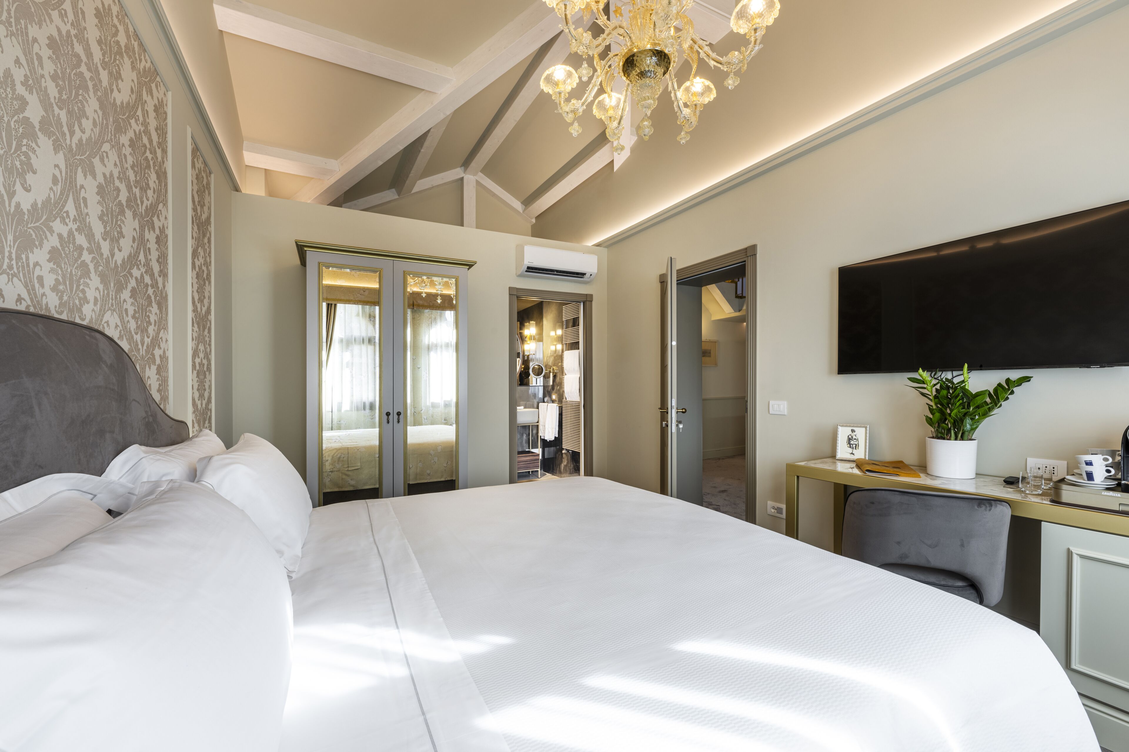 Ein modernes Hotelzimmer mit einem großen Bett, einem Schreibtisch, einem Flachbildfernseher, einer Zimmerpflanze und einem Kleiderschrank.