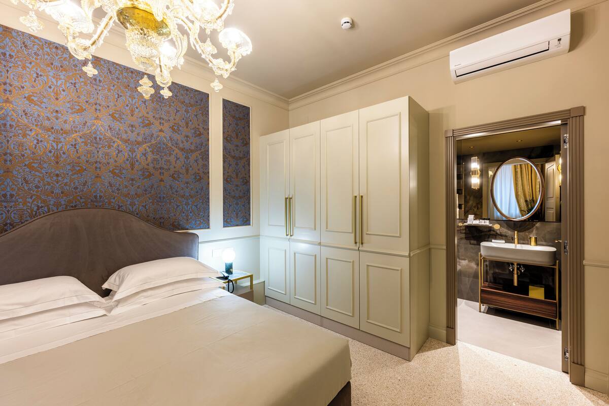 Une chambre avec un grand lit, une armoire et une salle de bain équipée d’un lavabo et d’un miroir.