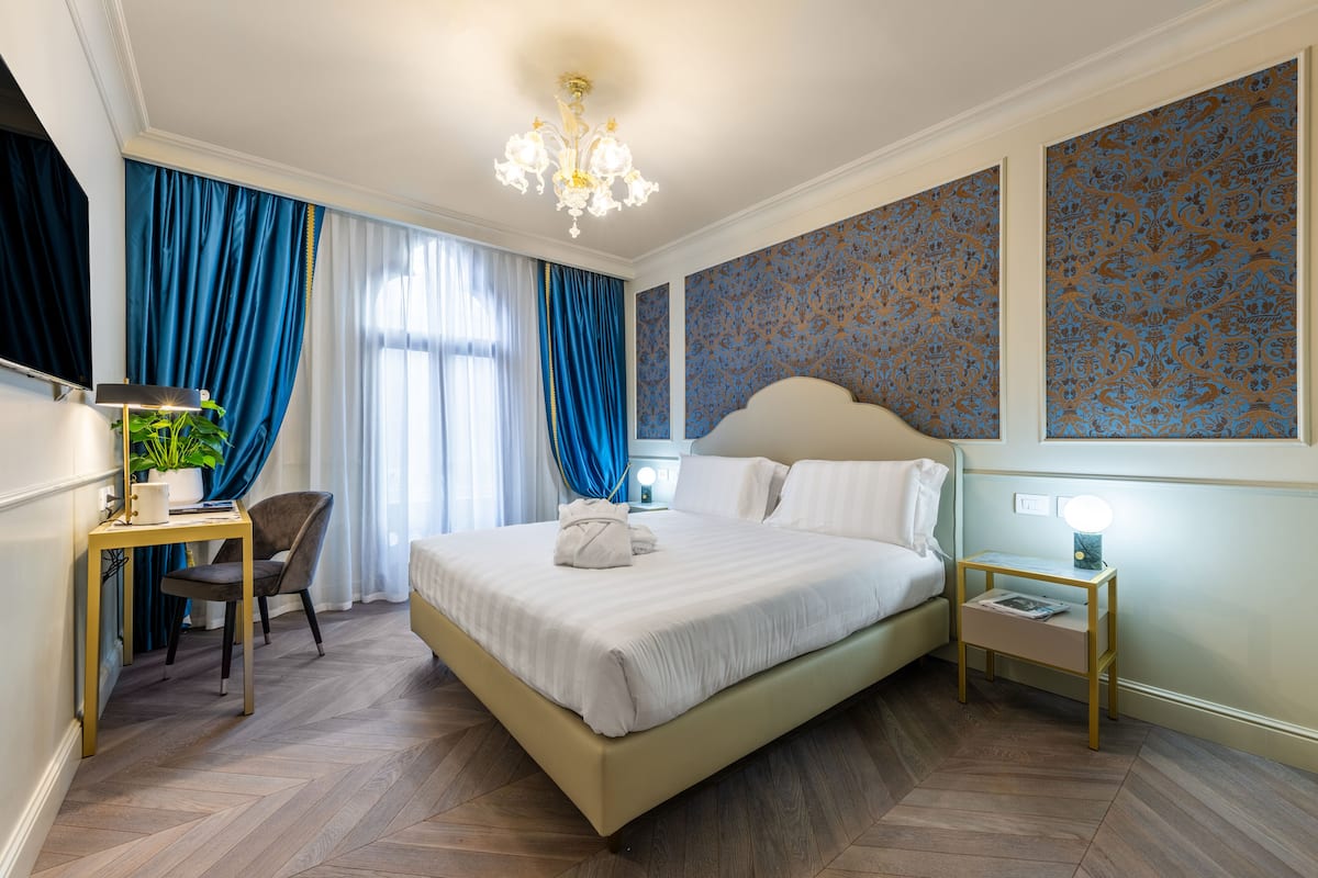 Une chambre d’hôtel avec un grand lit, un bureau avec une lampe, une chaise et une table de chevet avec une lampe.