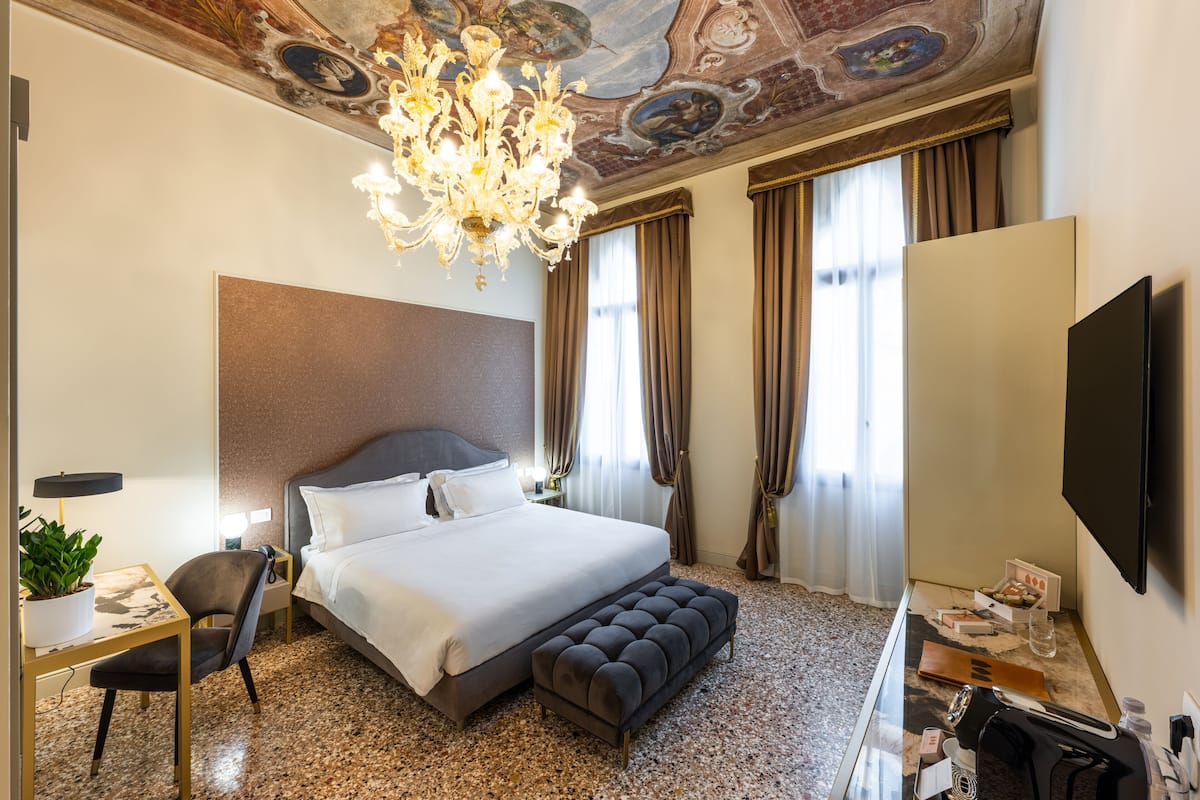Une chambre d’hôtel avec un grand lit, un bureau avec une chaise, une télévision et un lustre.