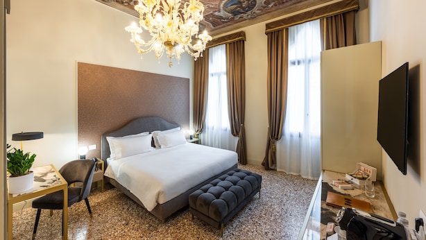 A hotel room with a large bed, a desk with a chair, a television, and a chandelier. - Hotel Palazzina Sardi (Venice)