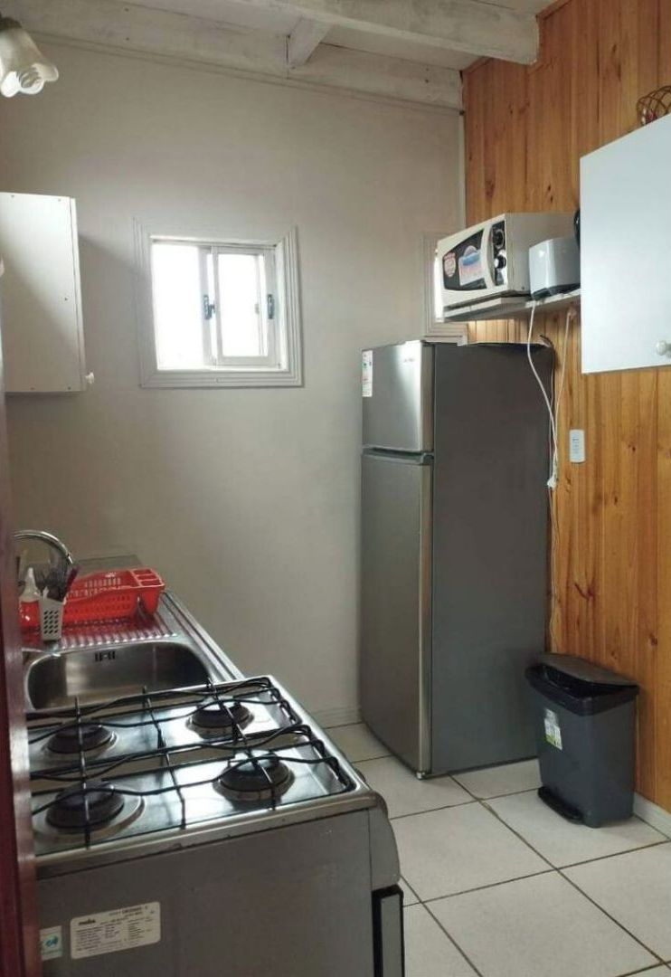 A compact kitchen with a gas stove, a stainless steel refrigerator, and a window providing natural light.