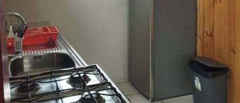 A compact kitchen with a gas stove, a stainless steel refrigerator, and a window providing natural light.