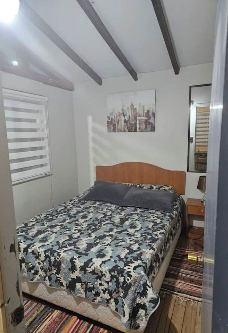 Une chambre à coucher avec un lit, une fenêtre avec des stores, un tableau représentant un paysage urbain et une tête de lit en bois.