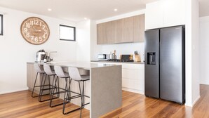 Eine moderne Küche mit einem Edelstahl-Kühlschrank, einer großen Holzuhr und einer Bar mit Hockern.