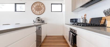 A modern kitchen with white cabinetry, a wooden floor, a large wall clock, and a stove with a microwave above it.