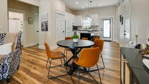 Een moderne keuken met witte kasten, een centraal eiland en een eethoek met een ronde tafel en oranje stoelen.
