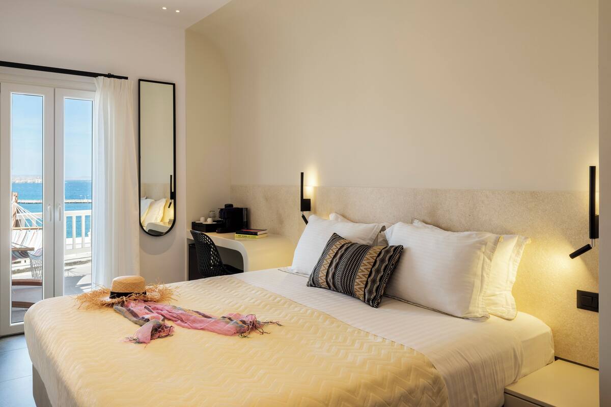 A hotel room with a bed, bedside table, and a view of the sea through a sliding door.