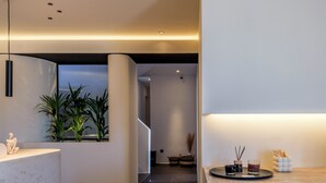 A modern interior with a curved reception desk, a seating area with a plant, and a bar area with drinks. - Yalos hotel sunset view  (Mykonos)