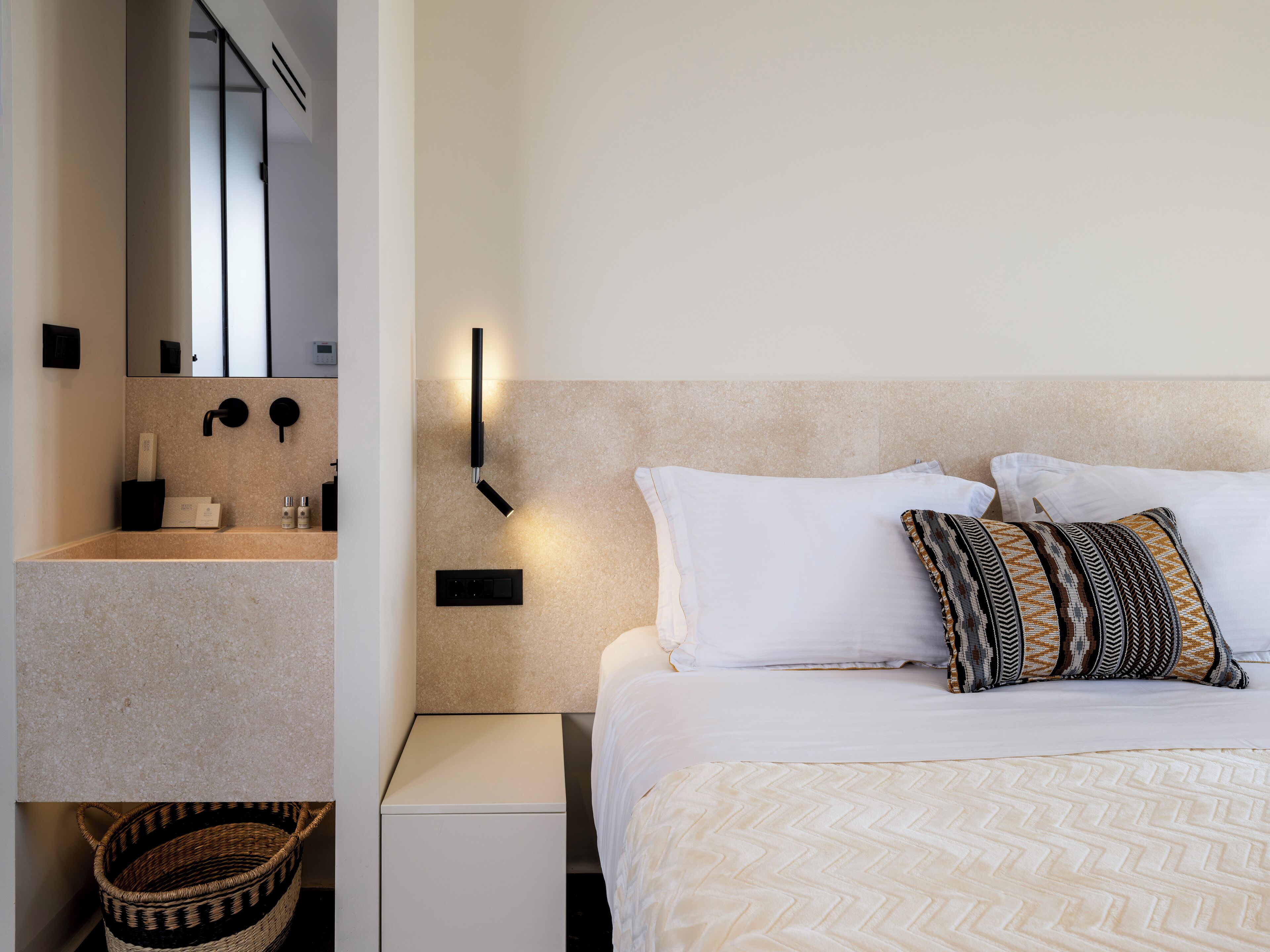 Ein modernes Hotelzimmer mit Bett, Nachttisch, Waschtisch und einer wandmontierten Leuchte.