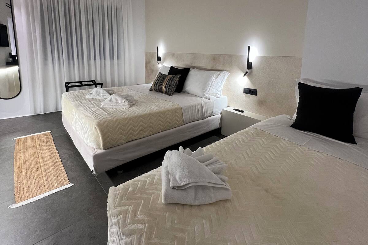 A modern hotel room with a large bed, a smaller bed, a bedside table, a mirror, and a window with curtains.