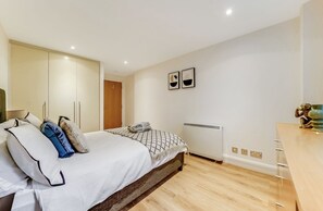 Une chambre à coucher avec un lit, une armoire, un radiateur et une petite table sur laquelle est posé un vase.
