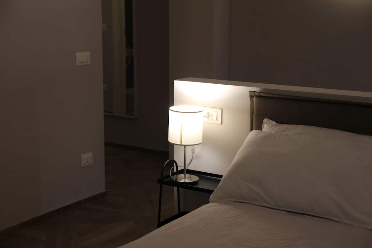 A neatly made bed with a white pillow and a bedside lamp on a small black nightstand.
