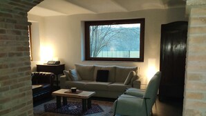 Una sala de estar acogedora con un arco de ladrillo, un sofá, una mesa de centro y vistas a árboles a través de un ventanal grande.