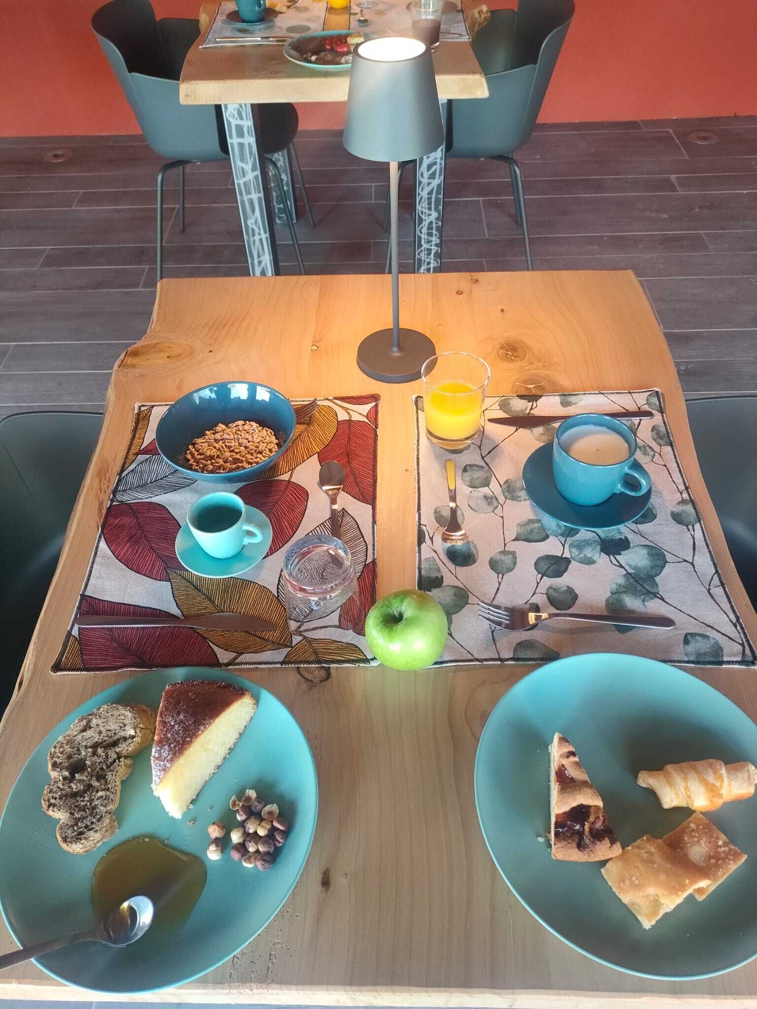 Une table à manger avec deux assiettes de nourriture, un bol de céréales, un verre de jus de fruits et une tasse de thé.