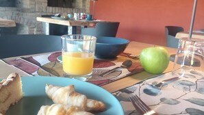 Desayuno con una fuente de cruasanes y una porción de pastel, un vaso de jugo de naranja y una manzana verde sobre una mesa.