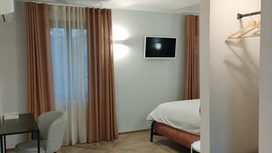 Una habitación de hotel con cama, escritorio con silla, televisor en la pared y perchero.