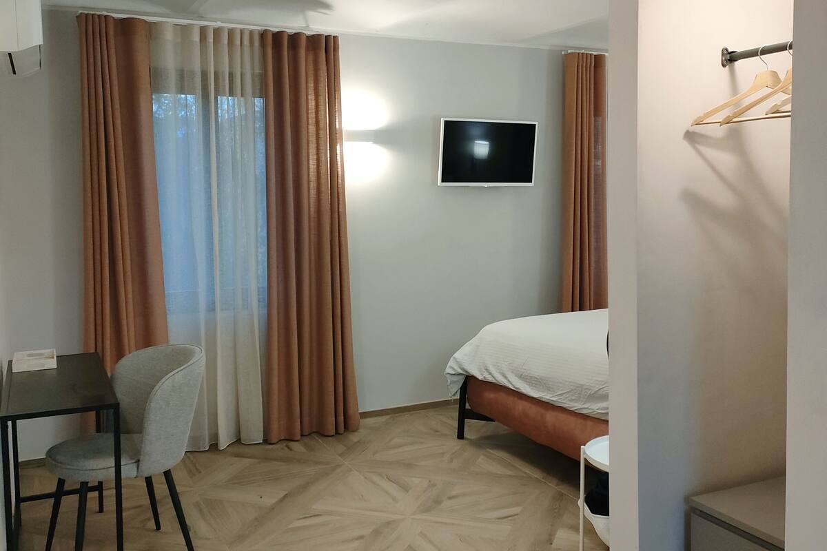 A hotel room with a bed, a desk with a chair, a TV mounted on the wall, and a coat rack.