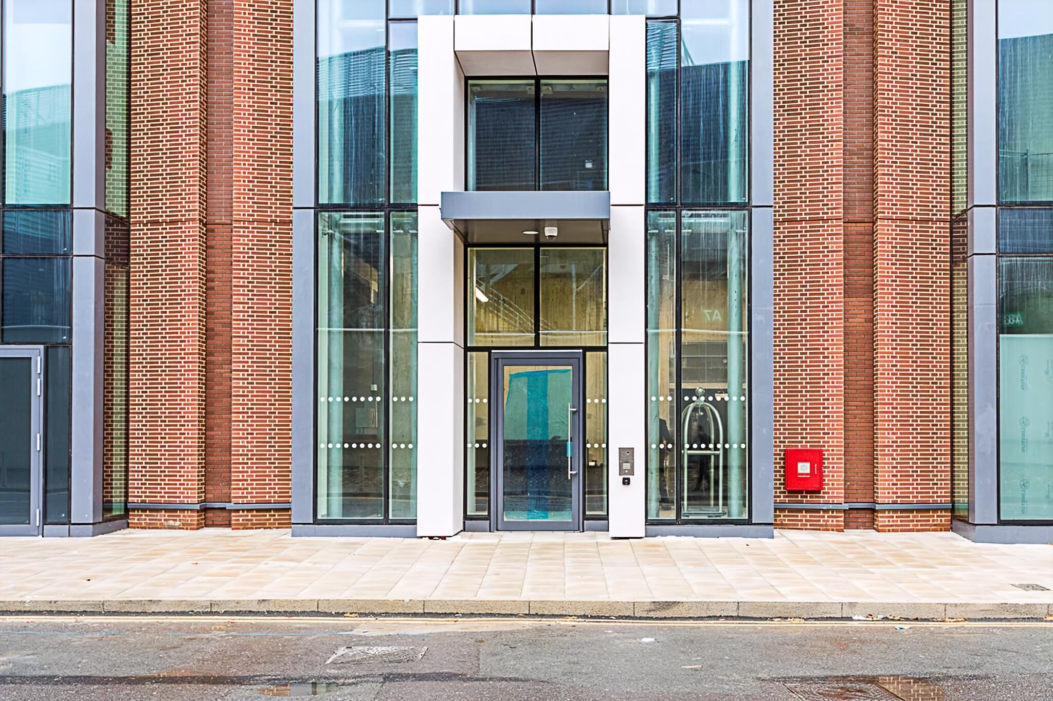 A modern building with a glass entrance, brick walls, and a tiled sidewalk.
