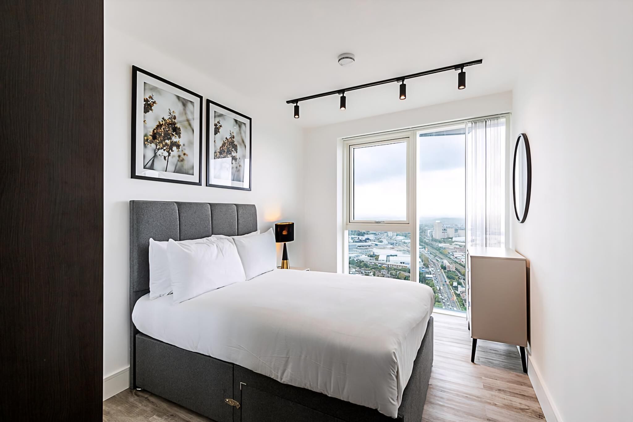 A modern bedroom with a large bed, a city view, and a minimalist design.