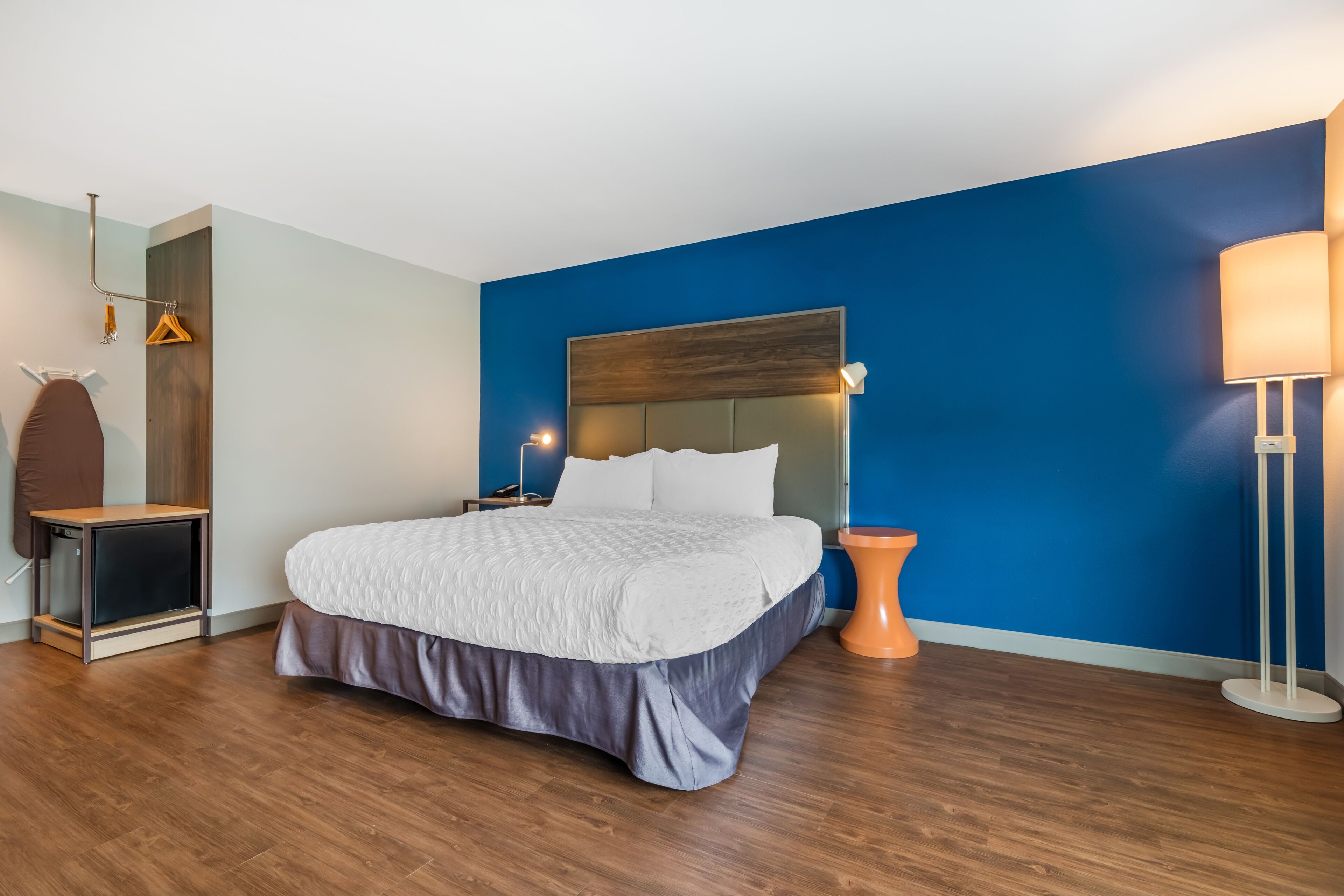 A modern bedroom with a large bed, a wooden headboard, a bedside table, a hanging coat rack, and a floor lamp.