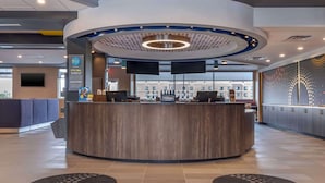 A modern hotel reception area with a curved counter, two monitors, and a view of the lobby.