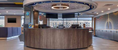 Un espace d’accueil moderne, avec un comptoir incurvé, deux écrans et une vue sur le hall d’entrée.