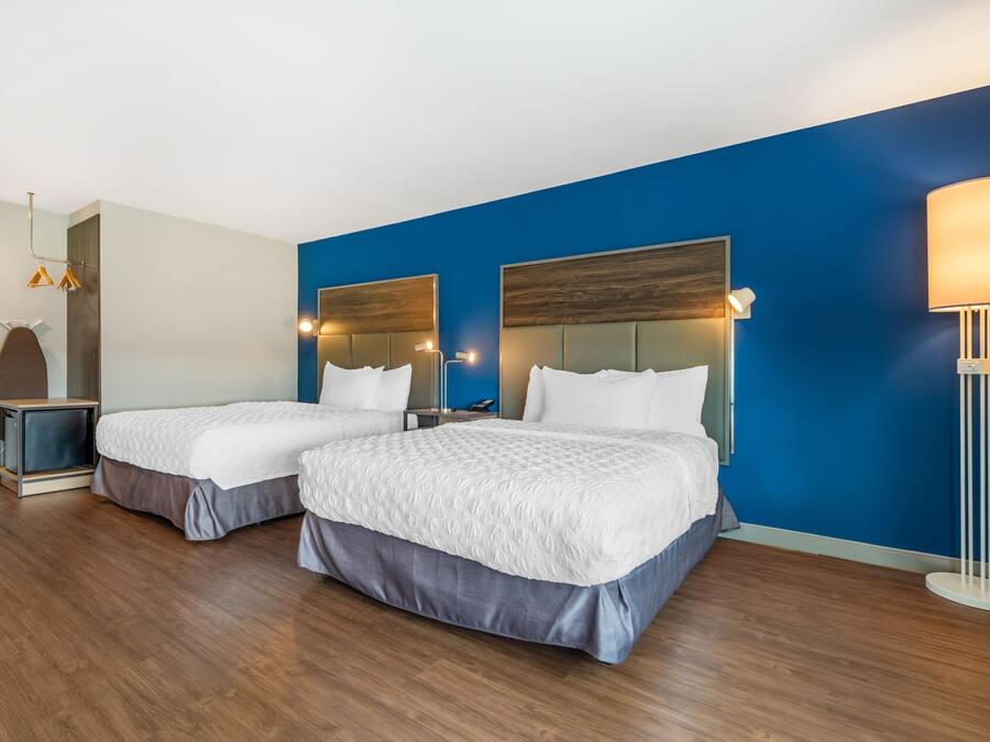 Une chambre d’hôtel avec deux lits, un mur d’accent bleu, une lampe moderne et une petite table d’appoint.