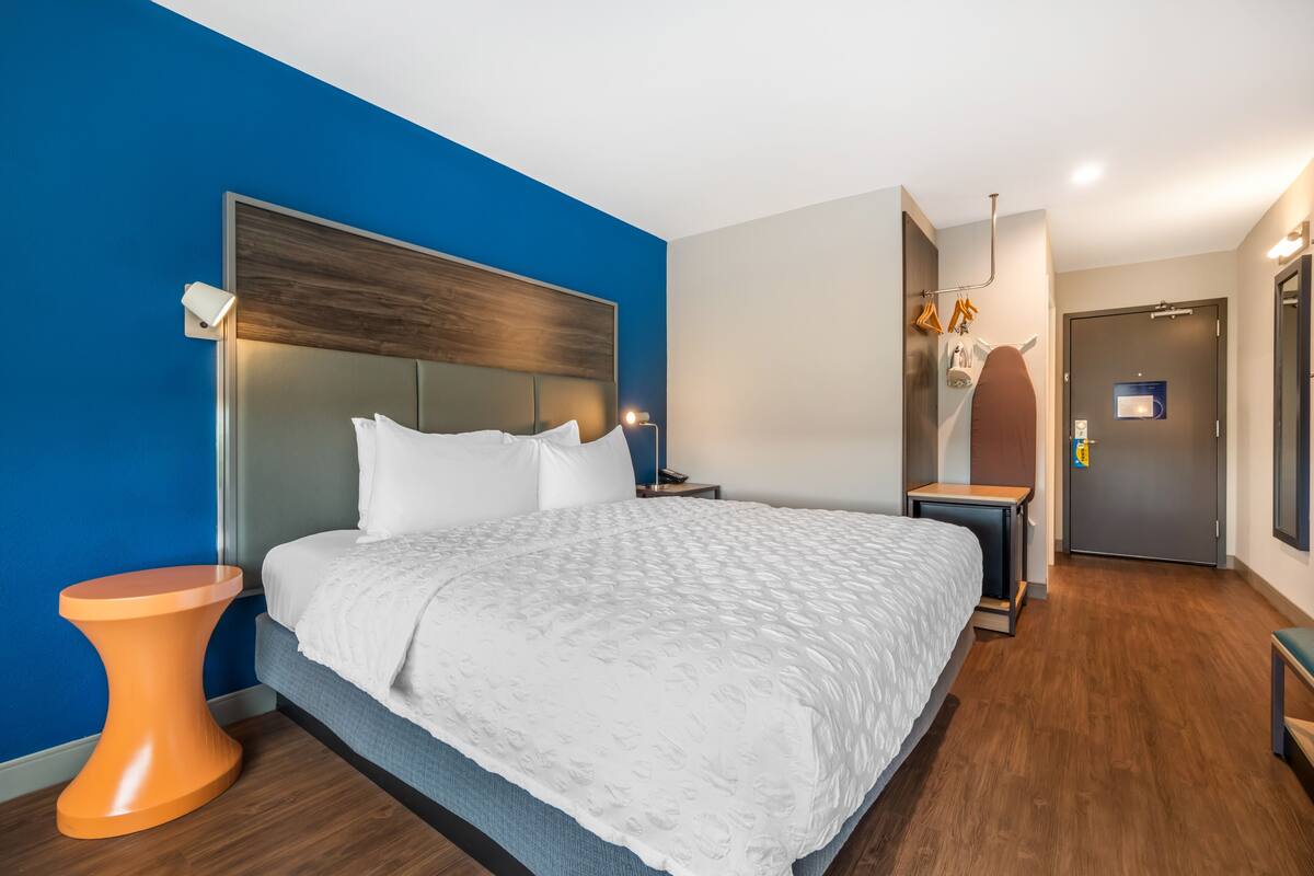 Een moderne hotelkamer met een groot bed, een nachtkastje, een kleine tafel en een deur naar de badkamer.