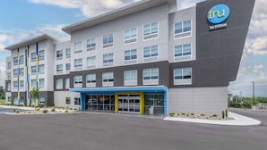 A modern hotel building with a blue and grey facade, multiple windows, and a prominent 'tru by Hilton' sign.