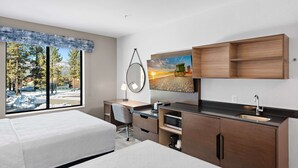 A modern hotel room with a large window, a desk with a chair, a bed, and built-in wooden shelves. - Hampton Inn Big Bear Lake (Big Bear Lake)