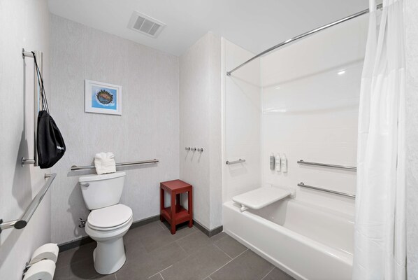 Un baño moderno con inodoro, un taburete pequeño rojo, una bañera con cortina de ducha y una barandilla.