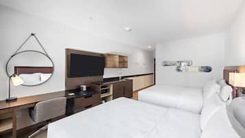 Ein modernes Hotelzimmer mit Bett, Schreibtisch, Stuhl, Fernseher, Spiegel und einer kleinen Küchenzeile.