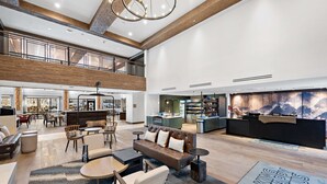 Um hall espaçoso com teto alto, uma mesa de recepção, área de estar com sofás e cadeiras, e vista para a área da cozinha.