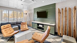 Uma sala de estar moderna com um sofá, poltronas de couro, uma televisão de tela plana e um painel decorativo de madeira.