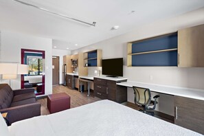 Habitación de hotel moderna con cama, escritorio, silla, televisor y estanterías integradas.