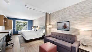 Quarto de hotel moderno com uma cama, um sofá, uma escrivaninha e uma janela com vista para árvores.