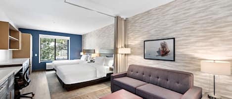 A modern hotel room with a bed, a sofa, a desk, and a window with a view of trees.
