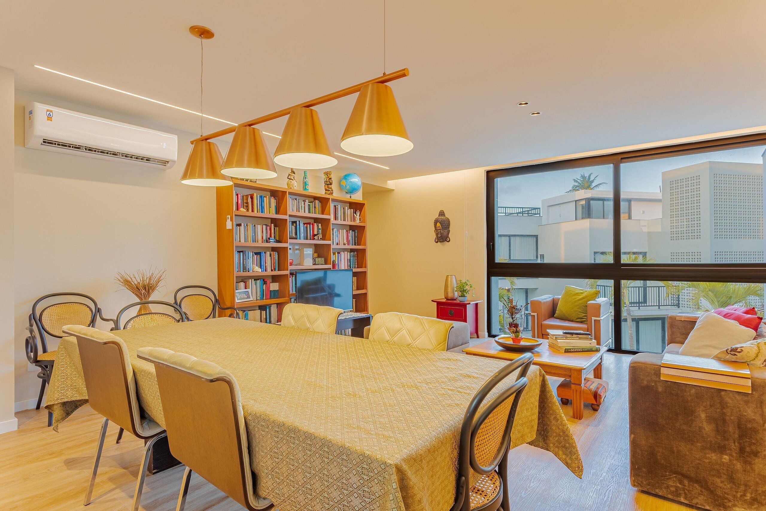 Uma sala de estar moderna com área de jantar, janelas amplas e uma estante de livros.