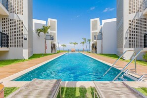Una piscina con sillones de descanso, palmeras y una vista despejada del océano.