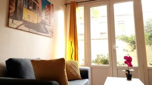 Une pièce comprenant un canapé, une table, une fenêtre avec des rideaux et un tableau accroché au mur.